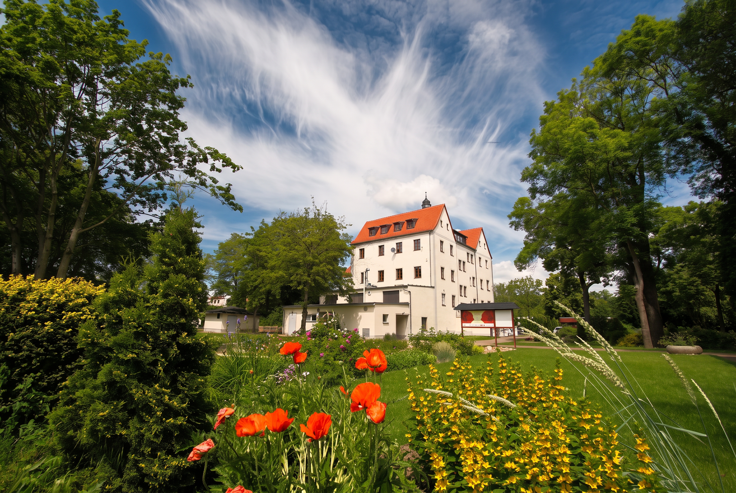 Rittergut Schenkenberg mit blühendem Garten und blauem Sommerhimmel