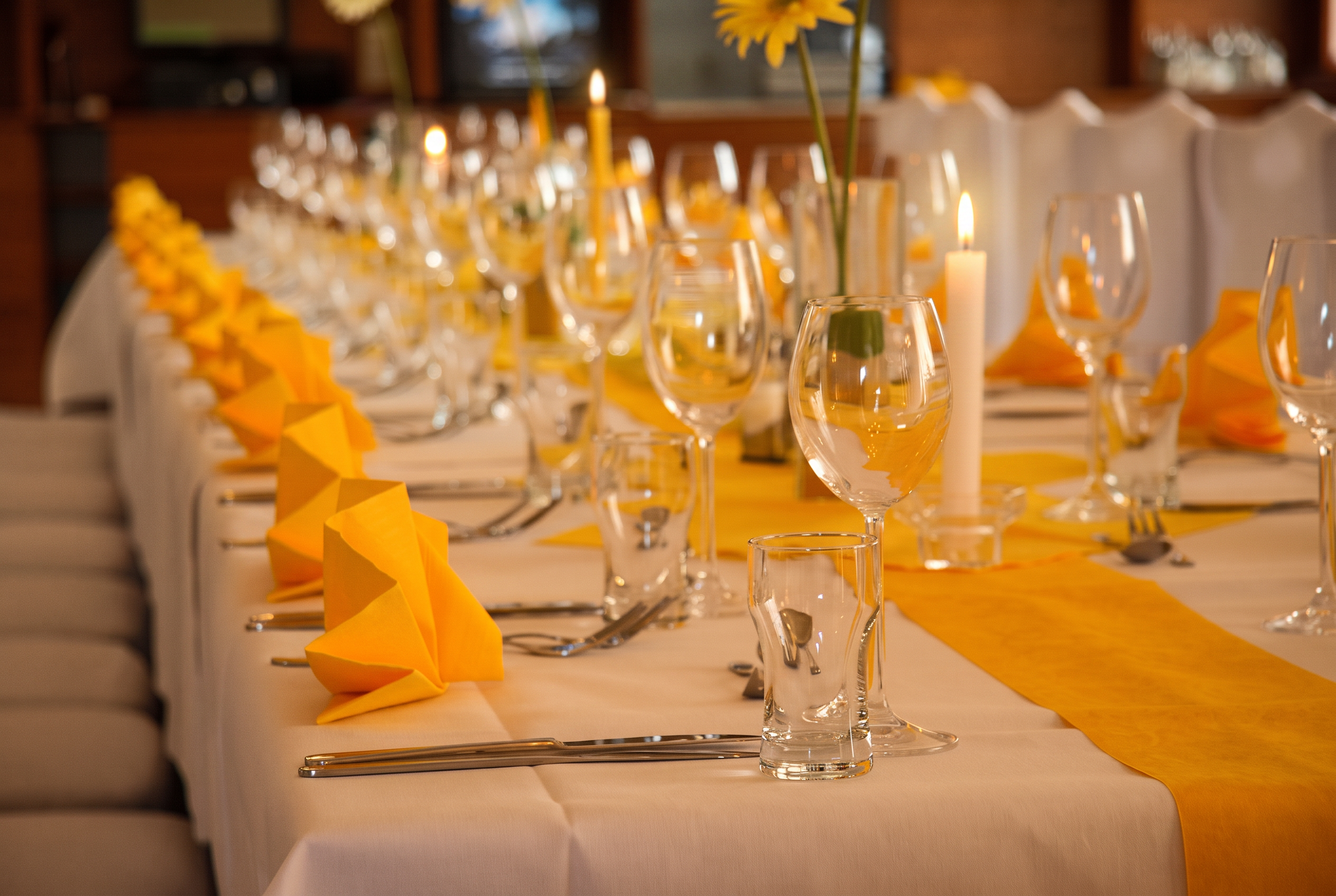 Lange Festtafel mit gefalteten gelben Servietten und Weingläsern